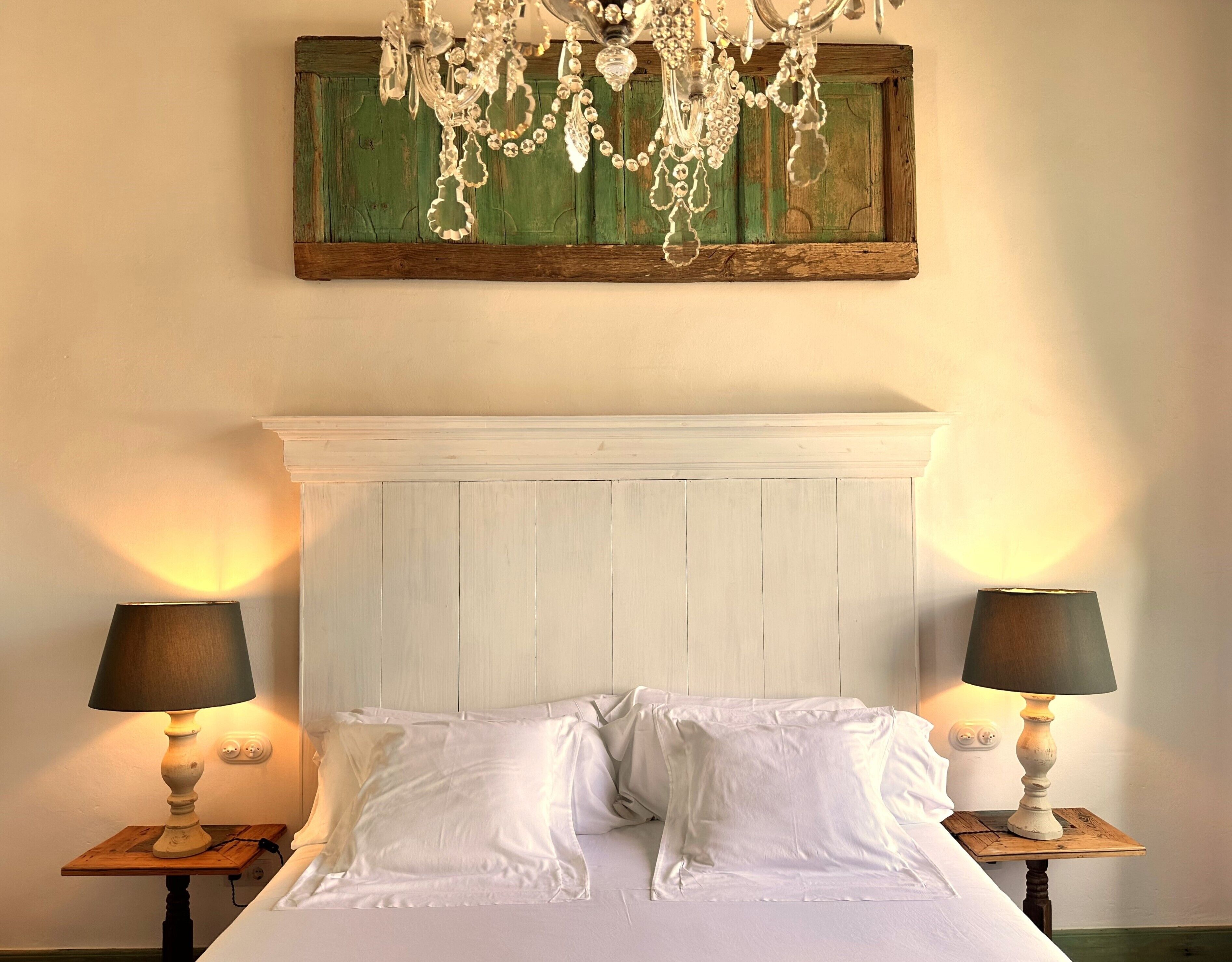 Un dormitorio con una cama blanca, dos lámparas de noche, una mesita de noche de madera, un cuadro con marco verde y un cabecero blanco.