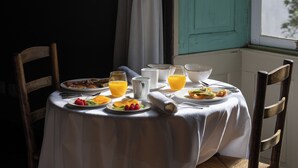 Een ontbijttafel gedekt met borden, glazen en een schaal, dicht bij een raam met een blauwgroene deur.