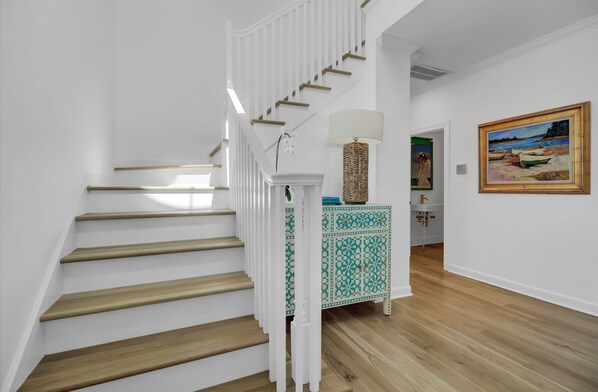 Uma escadaria com degraus de madeira e corrimãos brancos, uma mesa lateral estampada e um quadro na parede.