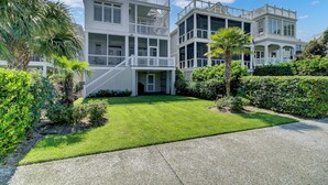A two-story beachfront property with a well-maintained lawn, a covered outdoor area, and a staircase leading to the upper floor.