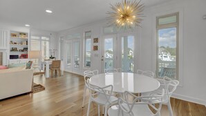 A spacious living room with a round white table and chairs, a white sofa, and a ceiling light fixture.