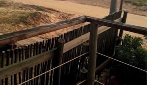A wooden balcony with a view of a sandy beach and a stop sign in the distance. - Chalet frente al  mar  Sta Monica  J Ignacio (Jose Ignacio Sta Monica)