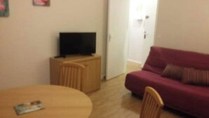 A living room with a TV on a wooden cabinet, a red sofa, and a round table with a magazine. - MERIDIEN-STUDIO 3* ALL-COMFORT (Dunkerque)