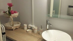 A bathroom with a white sink, a mirror, a glass shelf, a basket with flowers, and toiletries. - MERIDIEN-STUDIO 3* ALL-COMFORT (Dunkerque)