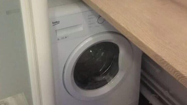 A compact laundry room with a washing machine, a wooden shelf, and a white door. - MERIDIEN-STUDIO 3* ALL-COMFORT (Dunkerque)