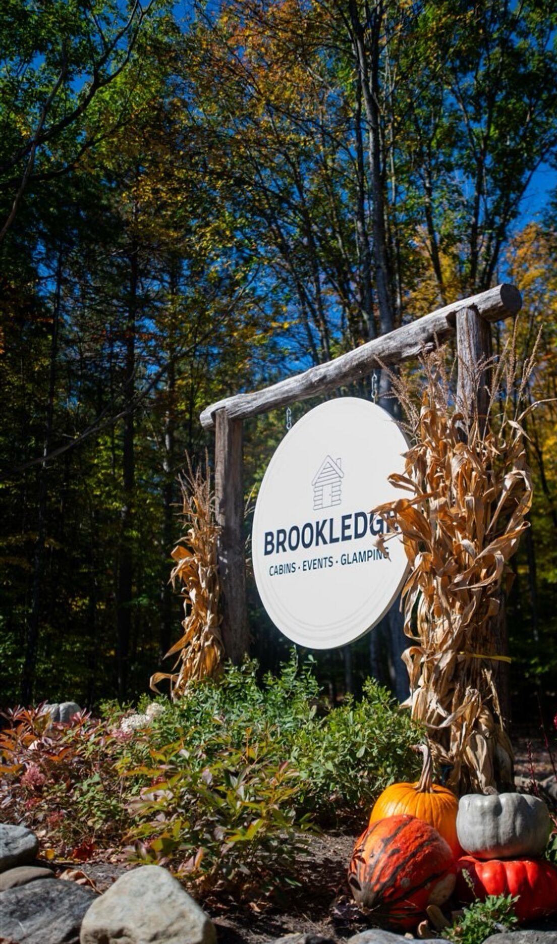 Señal para las cabañas, eventos y glamping de Brookledge, con un marco de madera rústica y un letrero circular blanco.