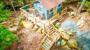 A cabin with a deck, surrounded by rocks and trees. - Cozy Cottage overlooking stream on 60 acres (Middle Grove)