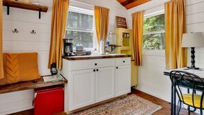 A cozy cabin interior with a wooden ceiling, white walls, a kitchen area with a red cooler, and a window with yellow curtains. - Cozy Cottage overlooking stream on 60 acres (Middle Grove)