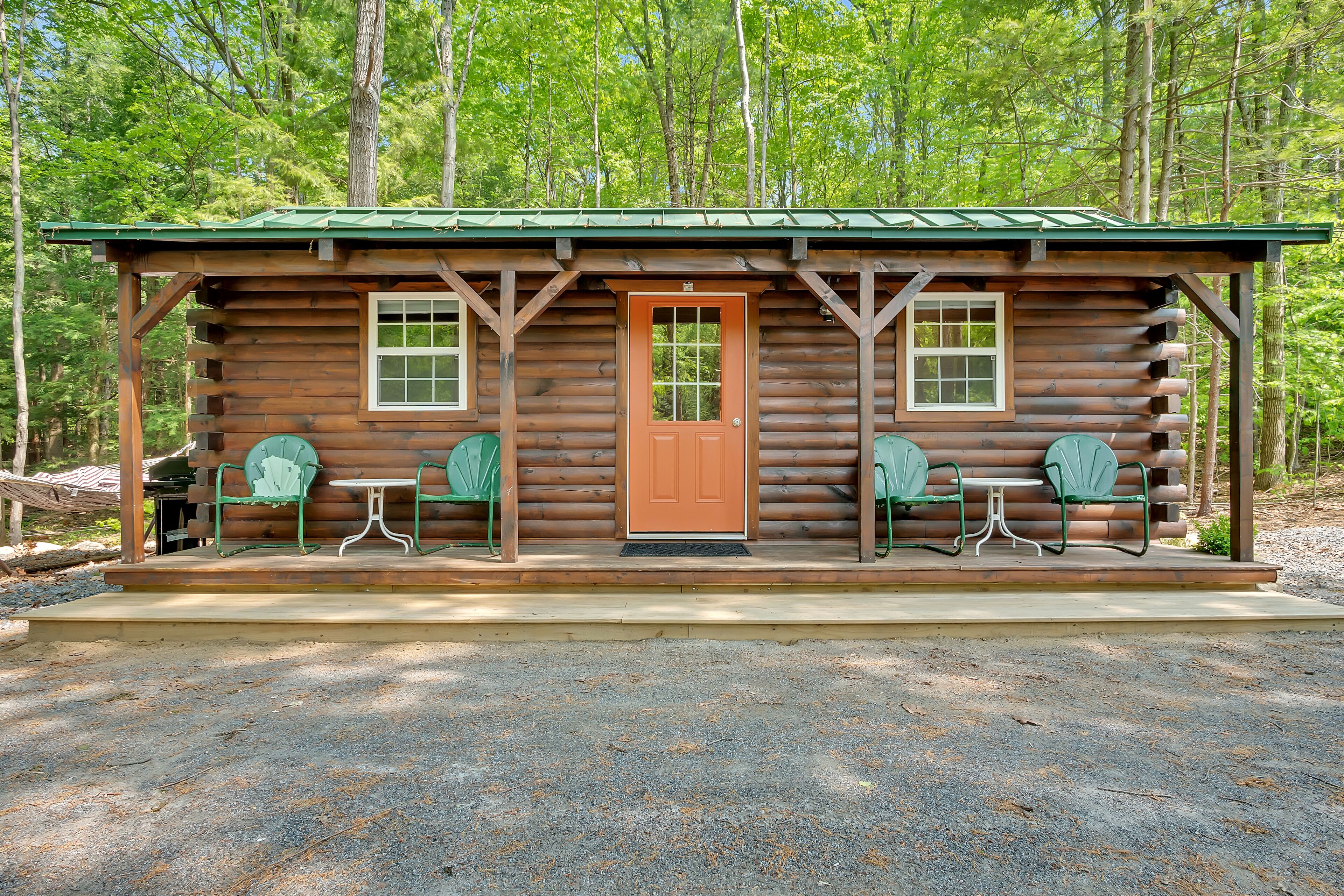 A log cabin with a porch, two windows, and two green chairs.