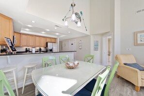 Een moderne keuken met houten kastjes, een wit aanrecht en een eethoek met een glazen tafel en groene stoelen.