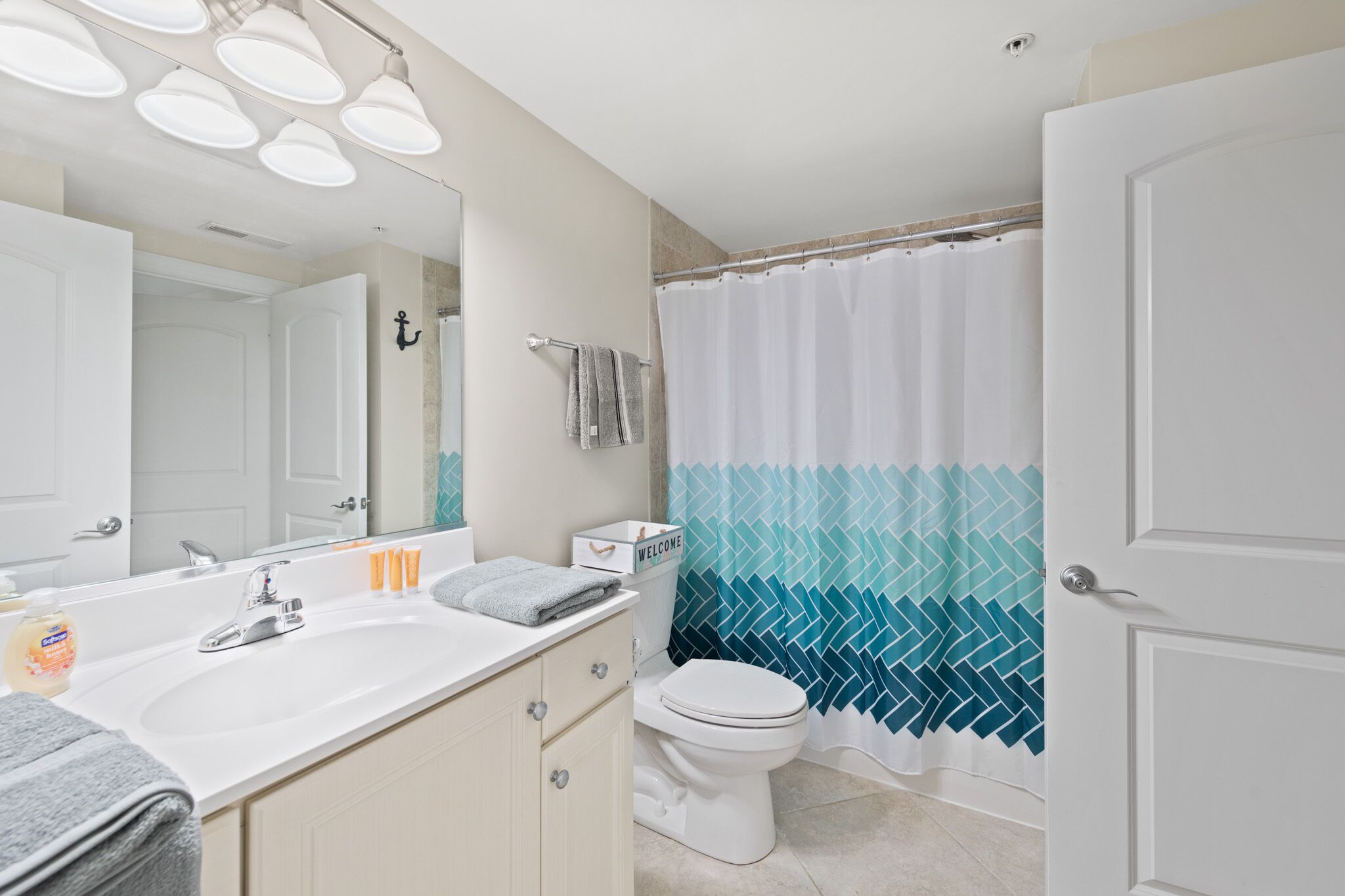 Un baño moderno con lavamanos, espejo y váter blancos. Hay una cortina de ducha con diseño azul y blanco.