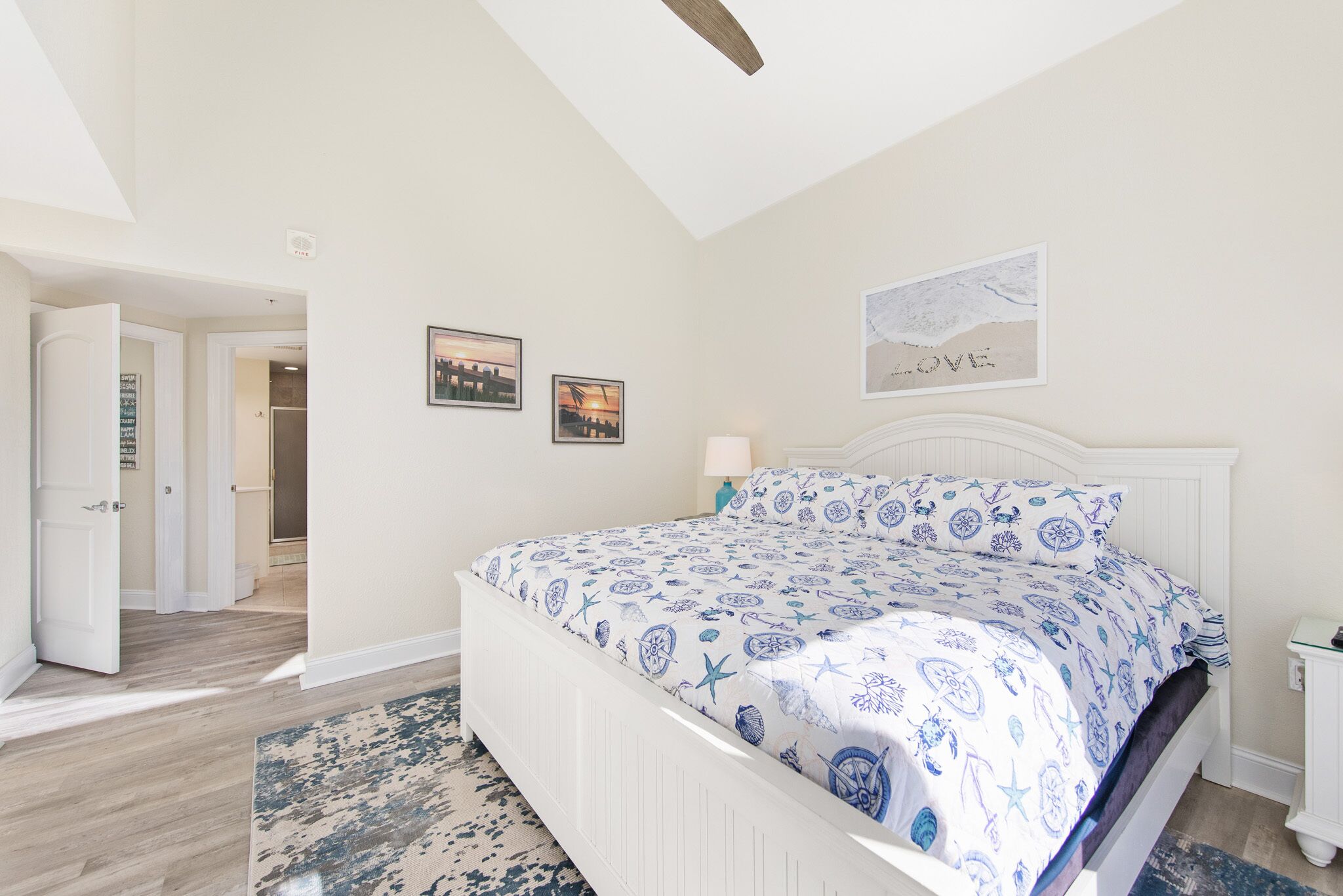 A bedroom with a white bed, a cityscape painting, and a beach-themed artwork.