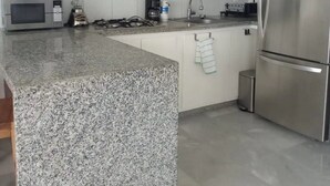 A modern kitchen with white cabinetry, granite countertops, stainless steel appliances, and pendant lighting. - CONDO FLAMINGO  BY TRVL2HM (Nuevo Nayarit)