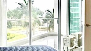 A bedroom with a large bed, a sliding glass door leading to a balcony, and a view of greenery outside. - CONDO FLAMINGO  BY TRVL2HM (Nuevo Nayarit)