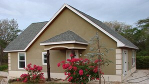 A single-story house with a gabled roof, a front porch, and a small garden with flowering plants. - American standart villa in the mountains overlooking the ocean (Colorado Abangares)