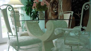 A dining area with white metal chairs and a glass-top table. There is a vase with flowers and a lion mural on the wall. - American standart villa in the mountains overlooking the ocean (Colorado Abangares)