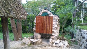 A stone structure with a wooden door, surrounded by greenery and a thatched roof. - American standart villa in the mountains overlooking the ocean (Colorado Abangares)