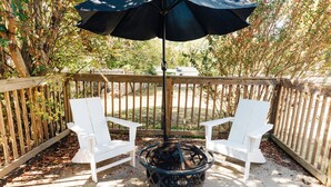 A deck with two white Adirondack chairs, a black fire pit, and a black umbrella providing shade.