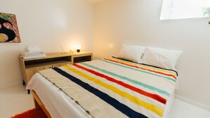 A neatly made bed with a striped blanket, a wooden nightstand with a lamp, and a red rug.