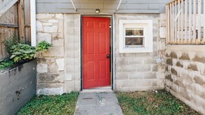 A red door with a small window above it, set in a stone wall with a wooden fence to the left.