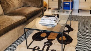 A living room with a brown sofa, a glass coffee table with books, a patterned rug, and a wooden cabinet with drawers.