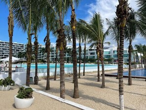 Un complexe hôtelier doté de plusieurs piscines, de palmiers et d’un bâtiment moderne avec des balcons.