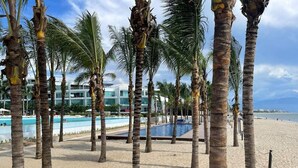 A beachside resort with palm trees, a swimming pool, and a beachfront view. - CONDO ARIAN  BY TRVL2HM (Bucerías)