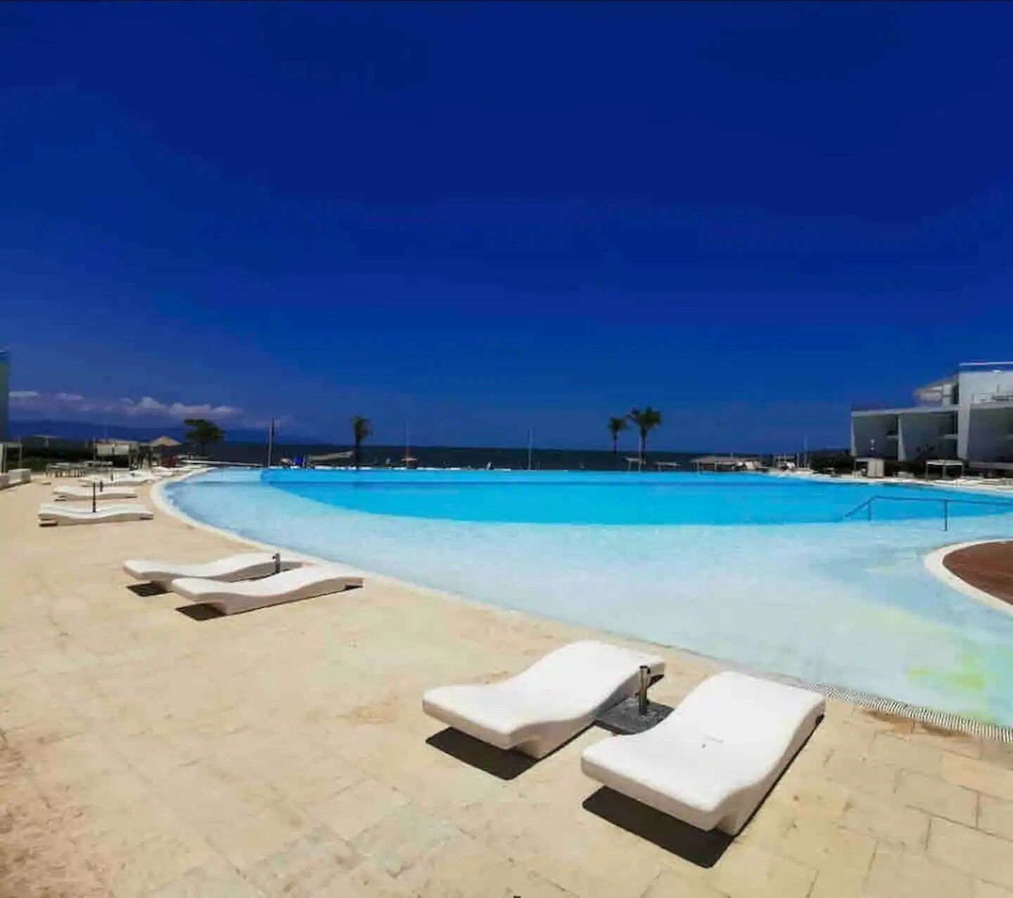 A poolside area with lounge chairs and a clear view of the ocean.