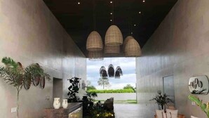 A modern reception area with a concrete reception desk, potted plants, wicker furniture, and hanging pendant lights. - CONDO ARIAN  BY TRVL2HM (Bucerías)