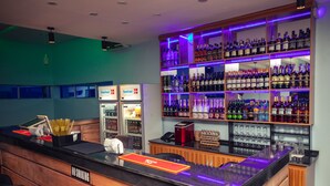 Uma área de bar com balcão, prateleiras cheias de garrafas de bebidas e dois refrigeradores com a marca 'Scanfrost'.