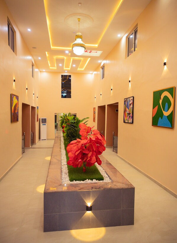 A hotel corridor with a central floral arrangement, recessed lighting, and artwork on the walls. - Beniks Courtyard Hotel (Ilorin)