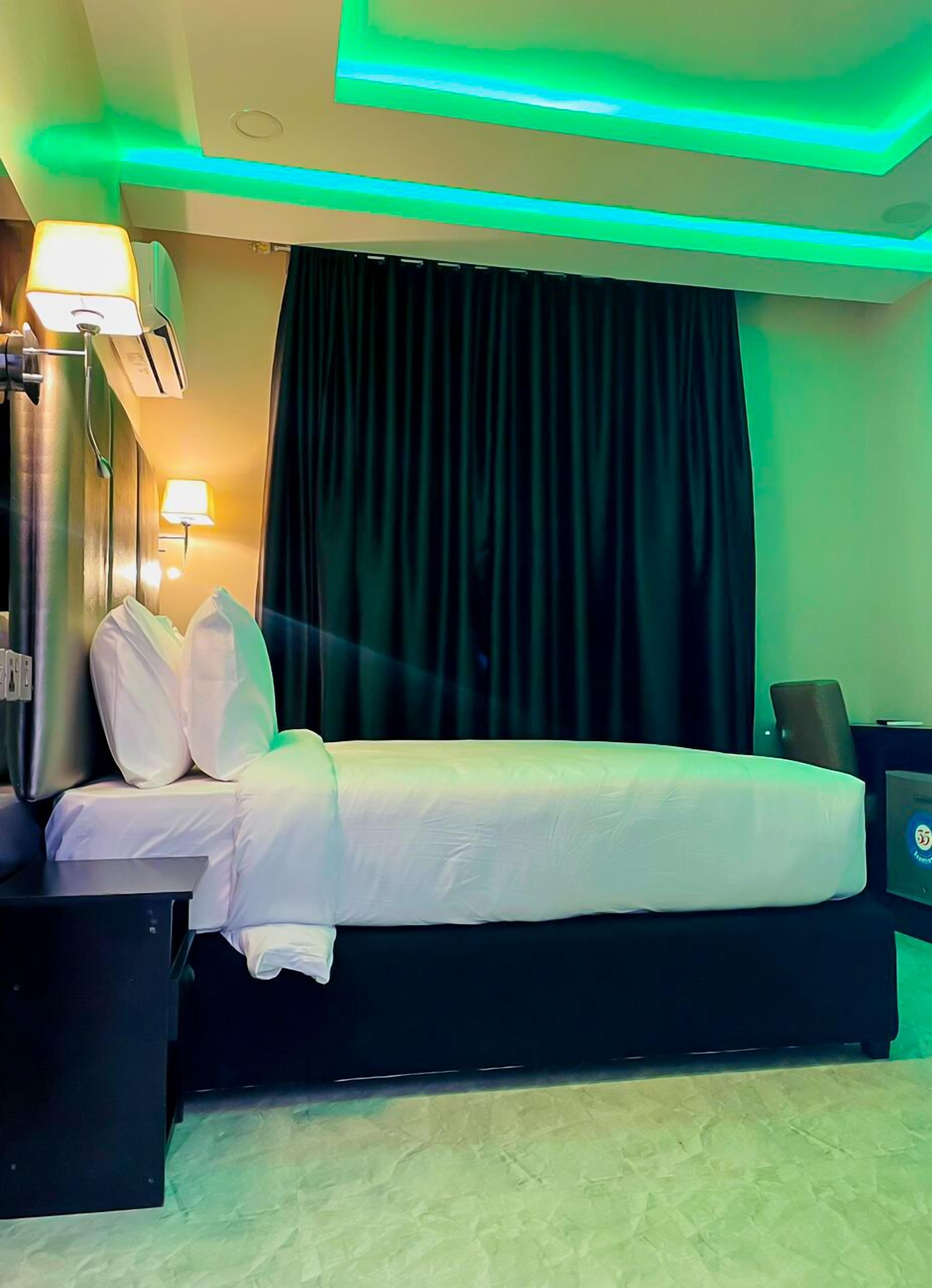 A hotel room with a bed, a nightstand, a lamp, and a curtain.