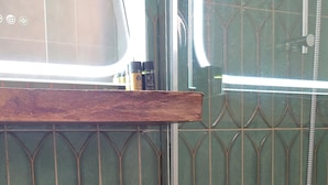 A bathroom with a white sink on a wooden countertop, green patterned tiles, and a shower with a hose.