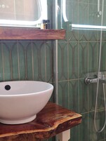 Un baño con un lavamanos blanco sobre una encimera de madera, azulejos estampados verdes y una ducha con manguera.