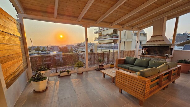 A balcony with a wooden ceiling, a green sofa, and a brick fireplace.