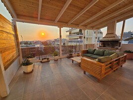 Un balcón con techo de madera, sofá verde y chimenea de ladrillo.