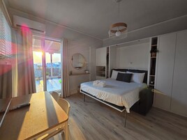 Un dormitorio con cama, escritorio, silla, armario y balcón con vistas.