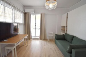 Una sala de estar moderna con una televisión de pantalla plana, piso de madera, un sofá verde, una silla blanca y una lámpara colgante.
