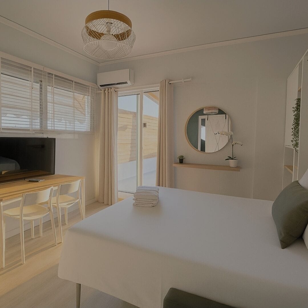 A modern bedroom with a bed, a desk, a TV, and a large window with curtains.