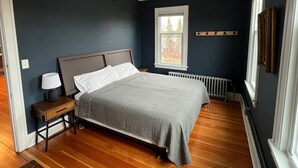 Een slaapkamer met een bed, nachtkastje, lamp, raam en een radiator.