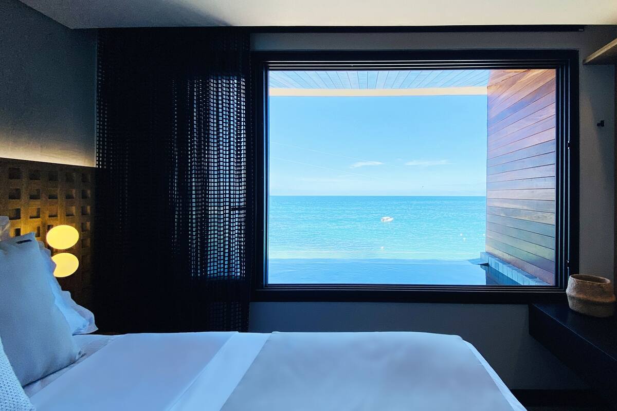Ein Hotelzimmer mit Bett, Fenster mit Meerblick und Nachttisch mit Lampe.