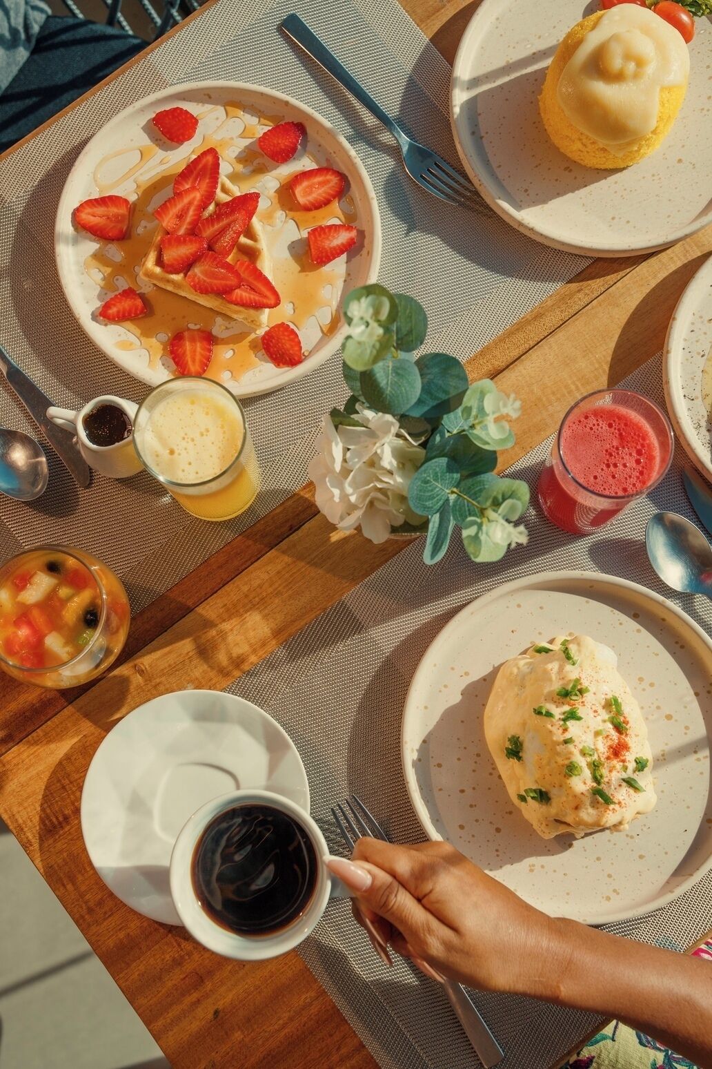 En frukostuppdukning med våfflor, frukt och drycker på ett träbord.