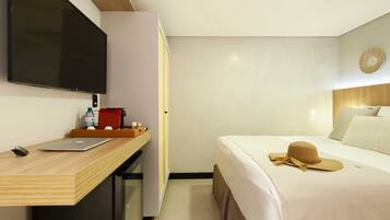 A hotel room with a bed, a desk with a laptop, a television, and a small table with a bottle and a red box.