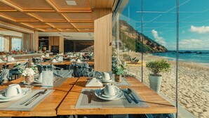 A restaurant with tables set for dining, a view of the beach, and a coastal landscape. - Pousada Antonella (Cairu)