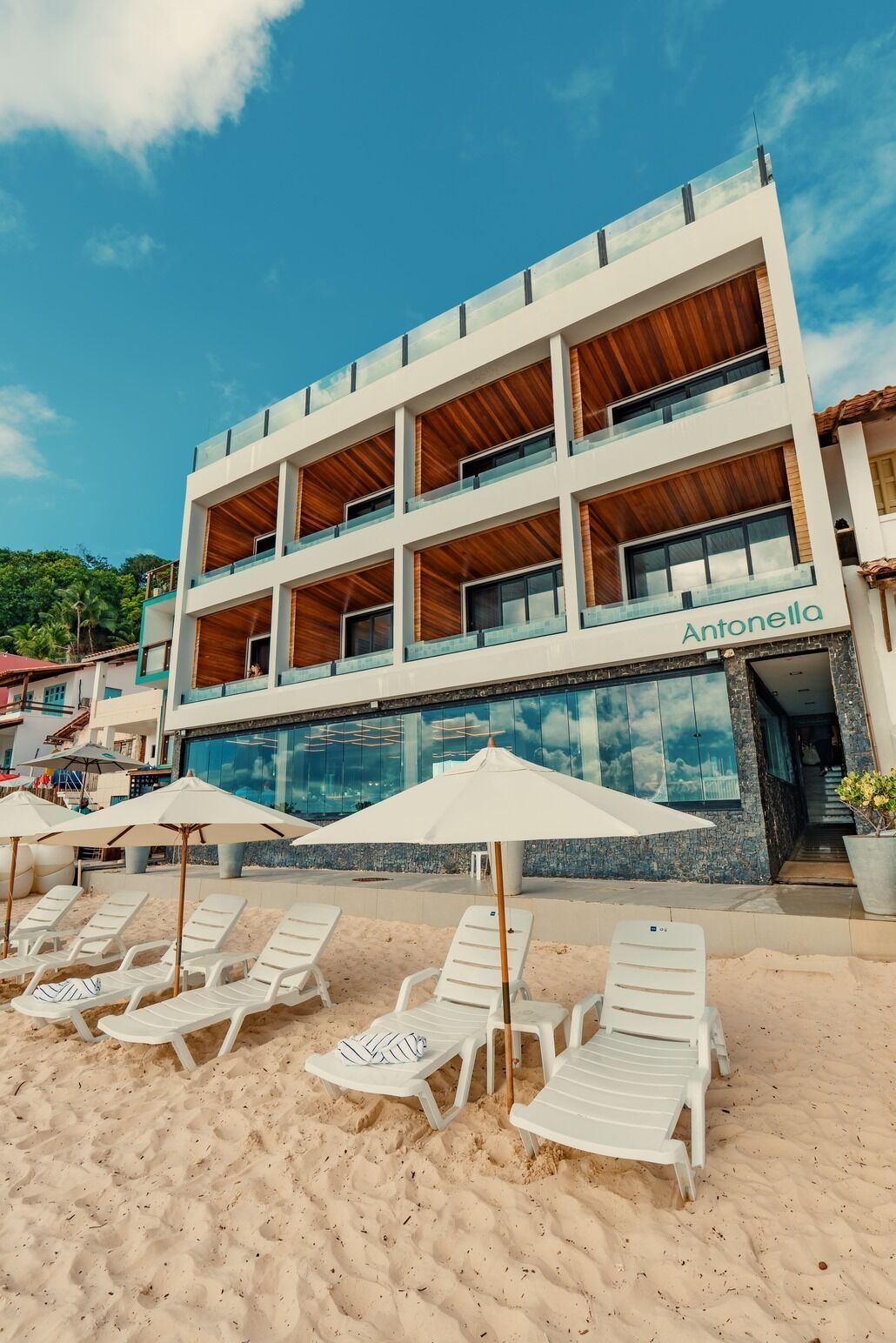 A hotel with a modern design, featuring a pool, multiple balconies, and beachside lounge chairs.