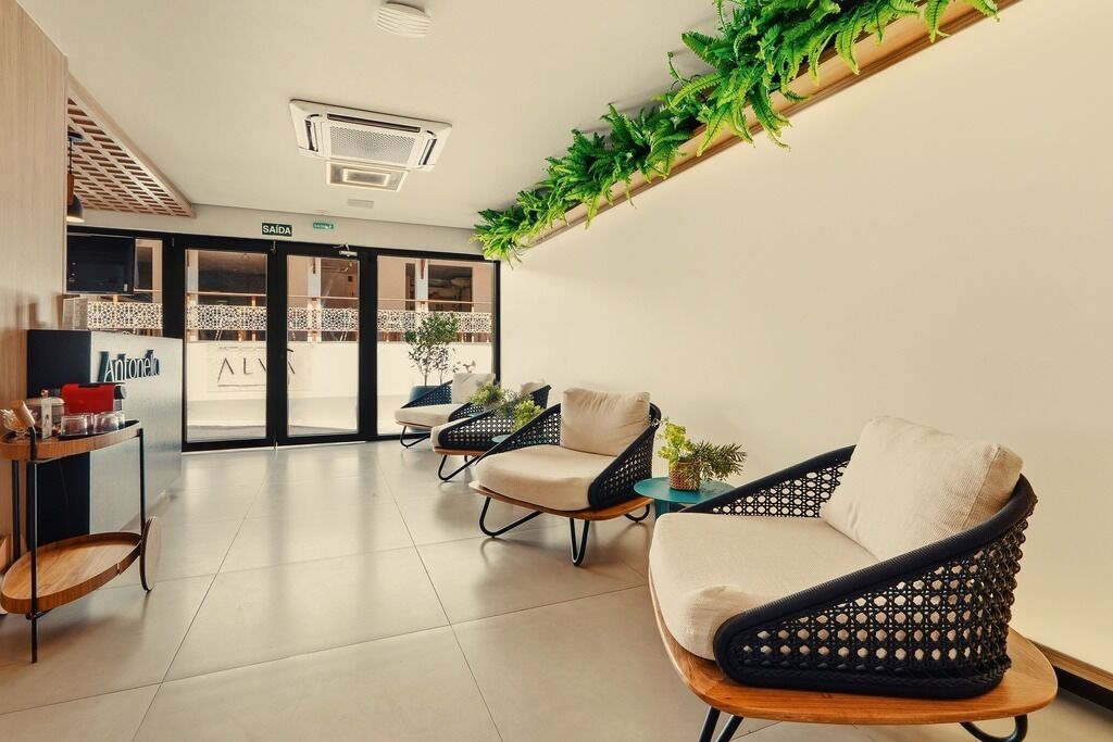 Un área de espera moderna con sillas de mimbre, una mesa de madera y una pared cubierta de plantas verdes.