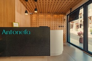 Una recepción con el nombre 'Antonella' en letras verde azulado, un techo de madera con diseño de cuadrícula y vistas a la calle.