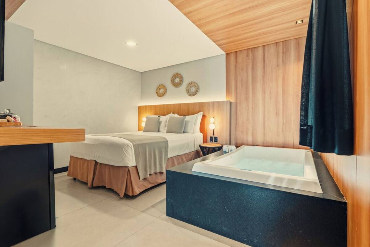 Ein modernes Schlafzimmer mit einem Bett, Nachttischen, einer integrierten Badewanne und einer Holzzahl.