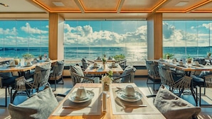 A dining area with tables set for two, large windows offering a view of the sea, and a ceiling with recessed lighting. - Pousada Antonella (Cairu)