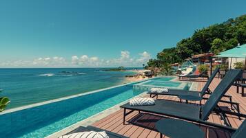 Un espace aménagé au bord de la piscine, avec des chaises longues et une vue sur l’océan.